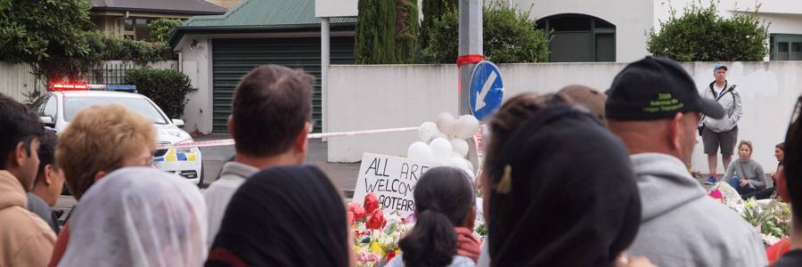 Women in veils console each other in front of a sign that reads 'All are welcome in Aotearoa' at the Deans Ave floral tribute to the victims of the March 15th terror attacks. James Dann via Wikimedia Commons