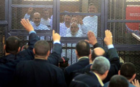 Men in suits wave to men in white behind bars in Egypt.