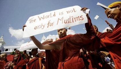 A Buddhist Monk at a demonstration holds up a sign reading 'The World is not only for Muslims'.