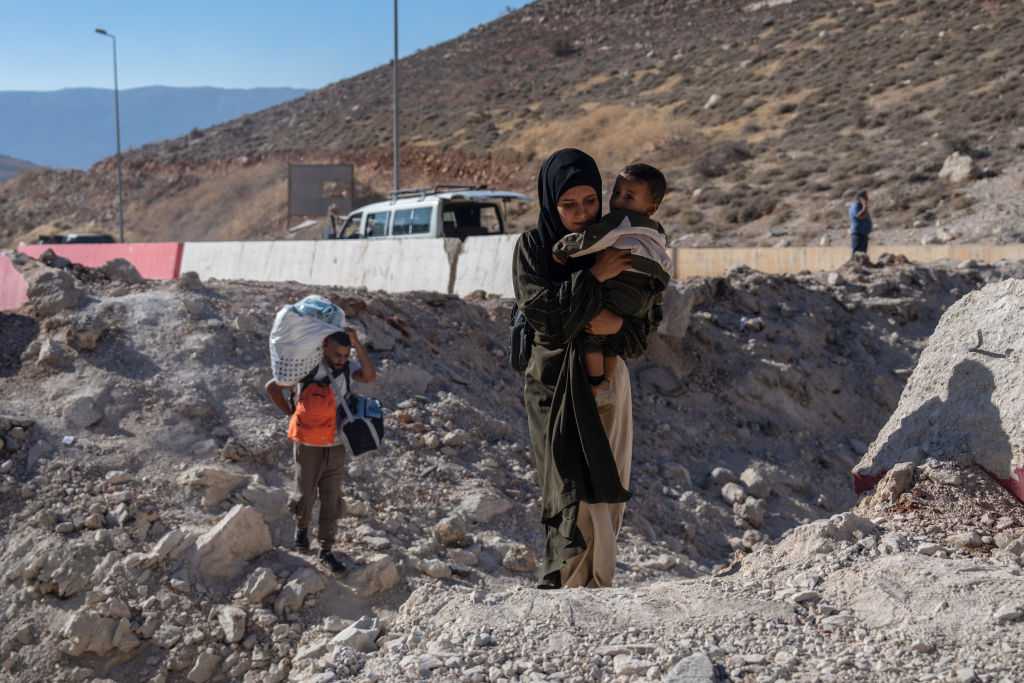 A woman carries a child through the crater from an Israeli air strike as she makes her way across the border from Lebanon into Syria on 5 October 2024. Photo: Getty Images