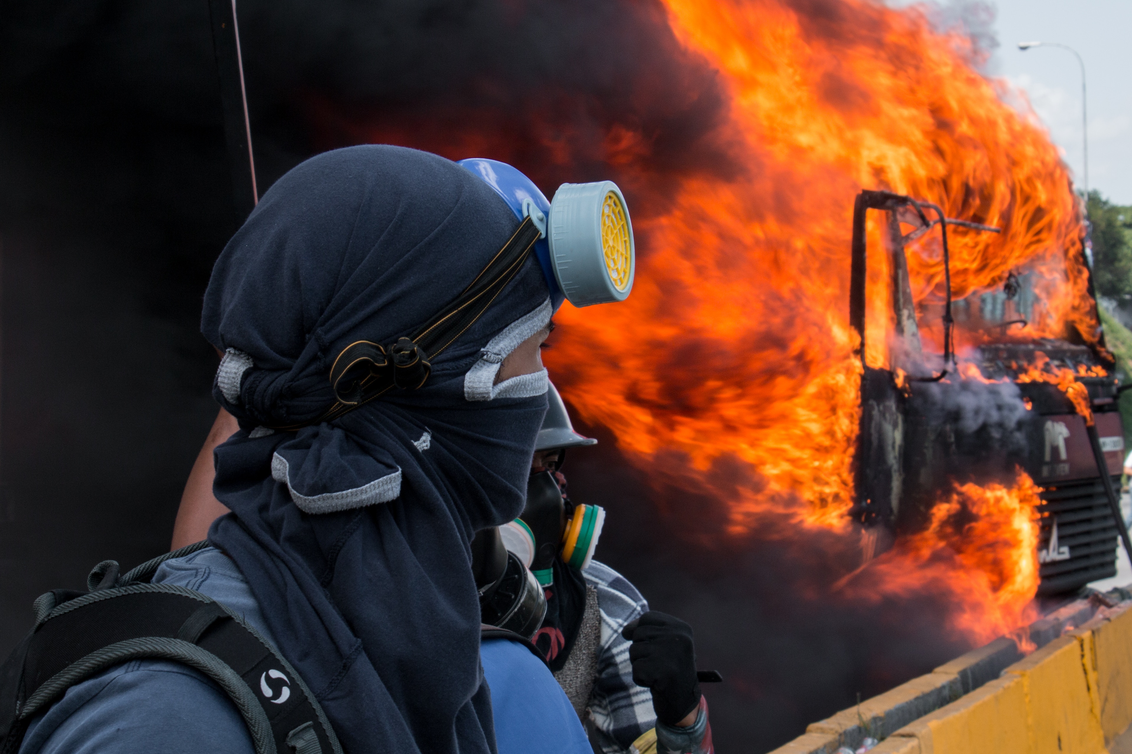 A protestor watching a burning vehicle in Caracas, Venezuela. PHOTO: Andrés Gerlotti on Unsplash (CC).